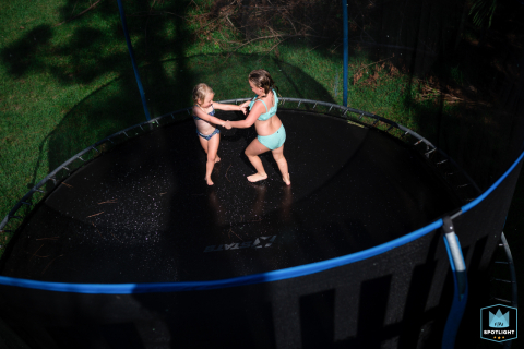 A high angle view captures Florida sisters playing on a trampoline in Sarasota, showcasing the perpetual summer vibe. Photo by a documentary family photographer.